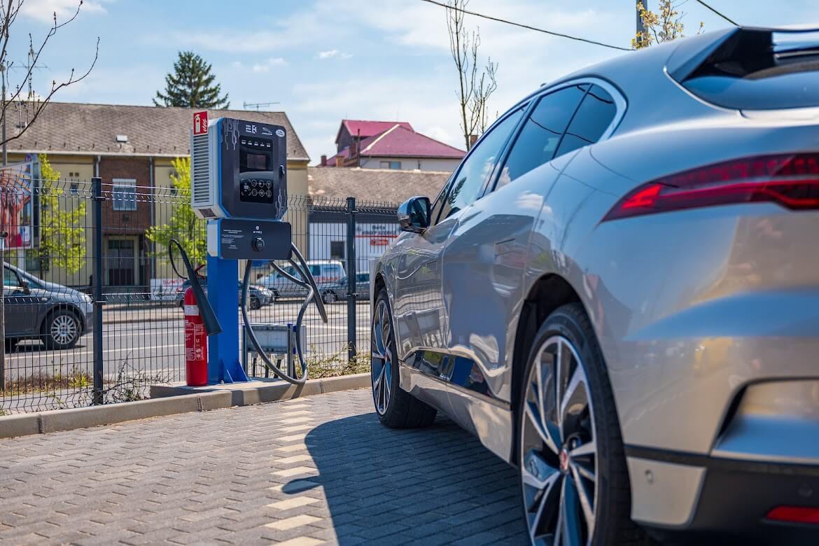 Elektromos autó töltése ALTE-GO töltőoszlopnál, napsütötte parkolóban